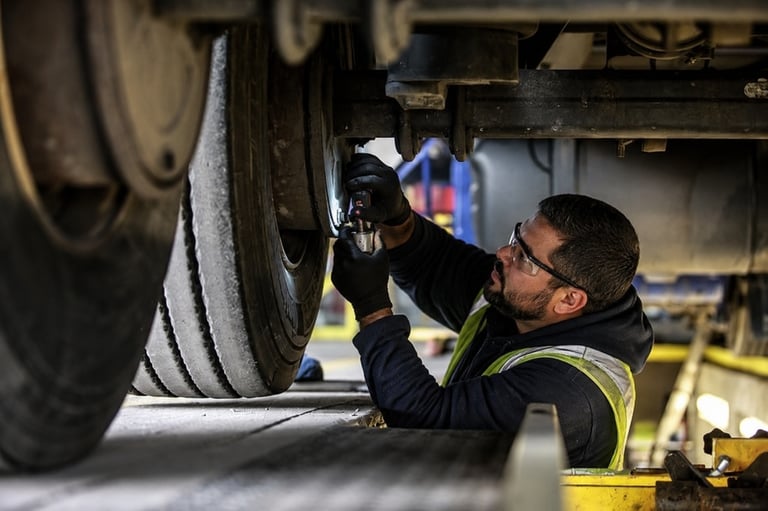 Mecânico usando óculos de proteção e luvas realizando manutenção no sistema de freios de um caminhão em uma oficina.