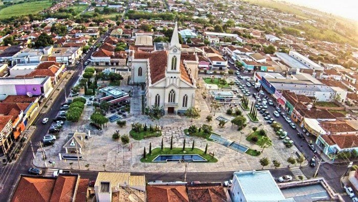 Vista aérea de uma praça central com uma igreja de arquitetura clássica ao centro, cercada por construções urbanas.