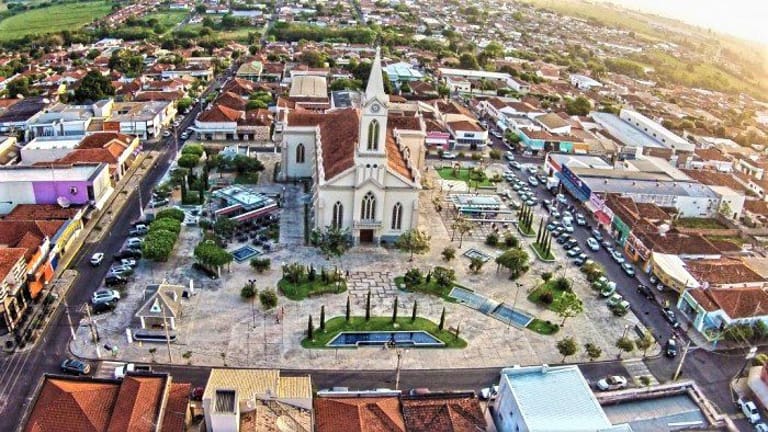 Vista aérea de uma praça central com uma igreja de arquitetura clássica ao centro, cercada por construções urbanas.